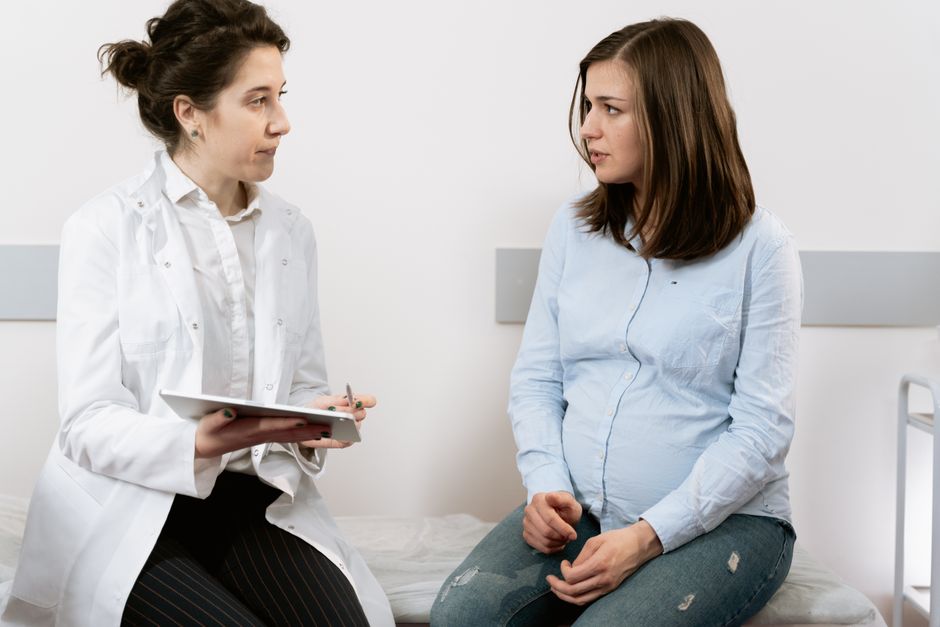 Pregnant woman consulting with a female OB-GYN doctor during a prenatal appointment in a medical clinic.