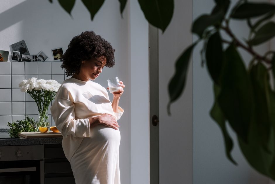 Pregnant woman drinking a glass of water in a sunny kitchen to stay hydrated during summer heat