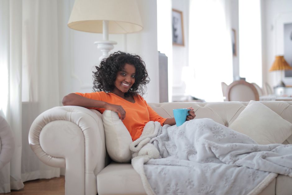 Woman resting comfortably on a sofa with a blanket and coffee mug, recovering at home after minimally invasive gynecologic surgery